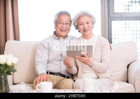 Happy old couple sitting on the sofa and using a tablet computer Stock Photo