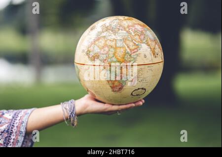 A female hand presenting a vintage globe in the blurred background; travel and explore the world Stock Photo