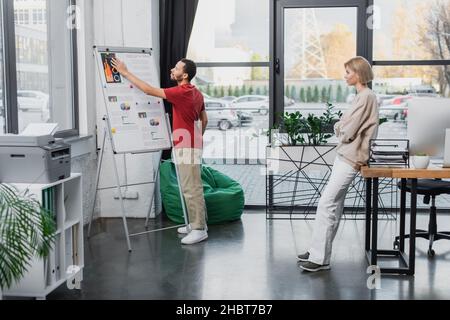 full length of african american man pointing at charts on flip chart near blonde colleague Stock Photo