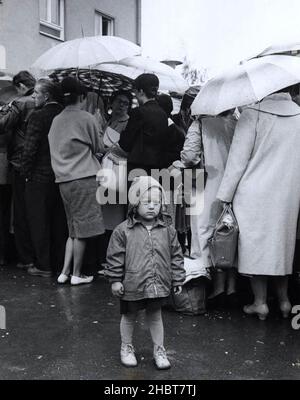 July 1961.  A 3-year-old East German girl waits in the rain as her parents line up to register at a refugee center in West Berlin Stock Photo