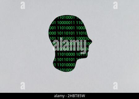 Silhouette of a human cardboard head cutout with a binary code made up of a set of green digits on a black background in its head Stock Photo