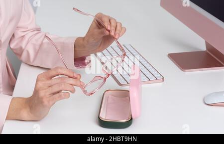 Salisbury, England, UK. 2021.  Womans hands removing glasses from case with back drop of computer and keyboard. Stock Photo
