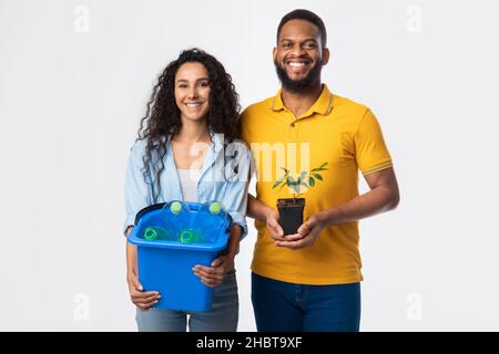 Couple Holding Plant And Plastic Bottles In Bucket, White Background Stock Photo