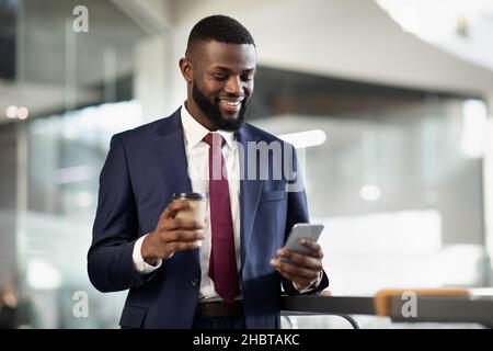 Cheerful black manager drinking coffee, using mobile phone Stock Photo