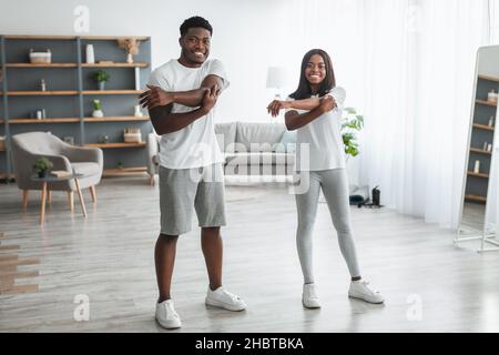 Young black couple doing arm stretch exercise together at home Stock Photo