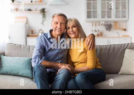 Loving Senior Couple Hugging Sitting On Sofa Posing At Home Stock Photo