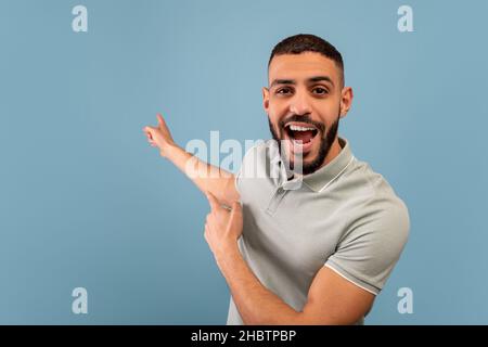 Overjoyed arab man showing blank space gesturing with hands, standing over blue background. Advertisement banner Stock Photo