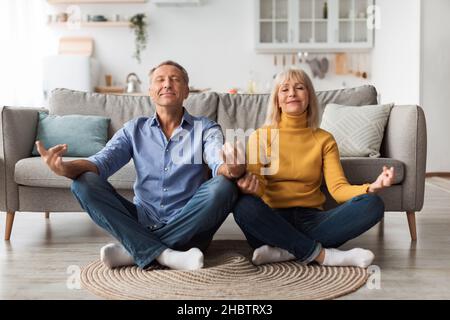 Senior Spouses Meditating With Eyes Closed Doing Yoga At Home Stock Photo