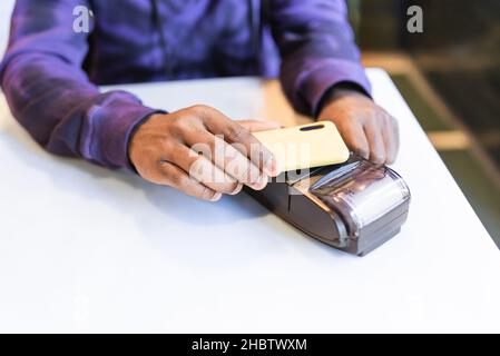 High angle of crop anonymous African American male client paying for order with cellphone through NFC technology on terminal in cafe Stock Photo