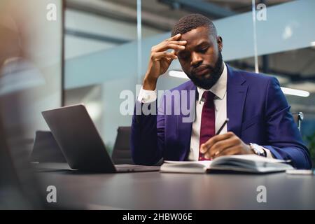 Pensive black man CEO working at office, taking notes Stock Photo