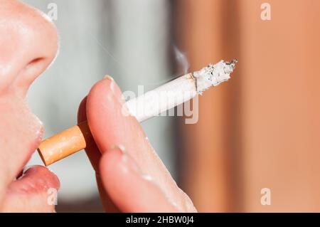 smoking woman: close-up of a woman's lips with a smoking cigarette between  the fingers Stock Photo