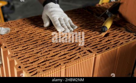 Industrial bricklayer worker placing bricks on cement while building walls. Close up of a man in protective gloves putting heavy brick block to form a Stock Photo