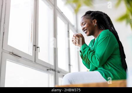 Young woman with cup of coffee looking out of window Stock Photo