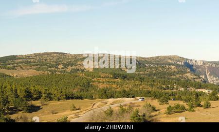 Aerial footage of a car riding on a road between green fields in the sun set. Shot. Drone flies over green hills and road with car fast driving. Aeria Stock Photo