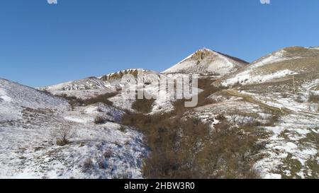Alps - aerial view. Mountains under the snow in winter. Panorama of snow mountain range landscape with blue sky. Stock Photo