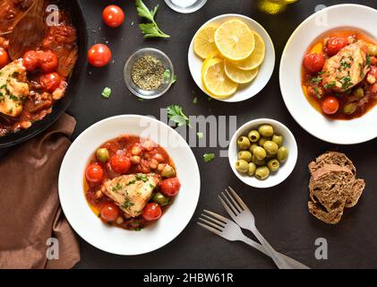 Cod stew with chickpeas, cherry tomatoes and olives over dark stone background. Top view, flat lay Stock Photo