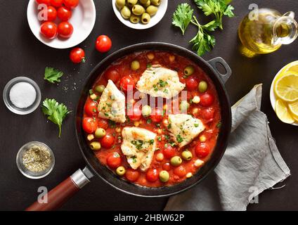 Cod stew with chickpeas, cherry tomatoes and olives in pan over dark stone background. Top view, flat lay Stock Photo