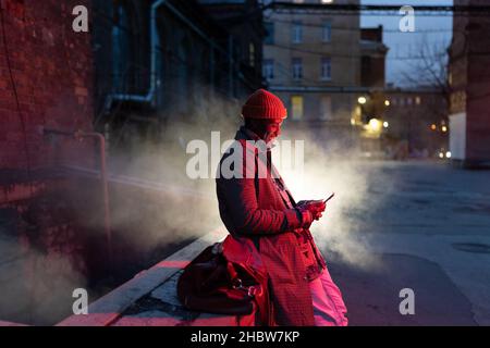 Smiling african man with smartphone on night street, black guy outdoors chatting in social media Stock Photo