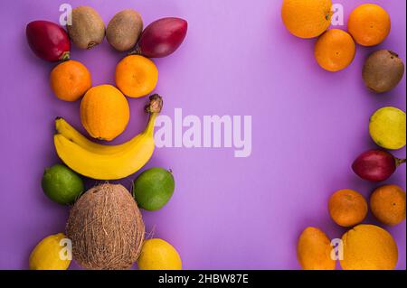 Citrus fruitage and bananas, coco, kiwi on purple background. Assorted citrus fruits and tamarillo. Coco on vintage table and other fruits. Copy space Stock Photo