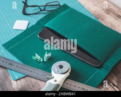 Creating a felt case for tablet, craft workshop. Green felt, a tablet, a cutting mat, a ruler, a rotary cutter, a tailor chalk and glasses on the wood Stock Photo