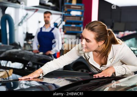 Female client closely examining car body after repainting in auto workshop Stock Photo