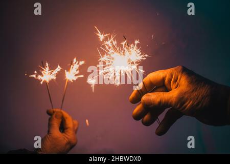 hands of elderly couple holding sparkles celebrating New Year Stock Photo