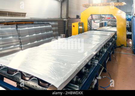 Conveyor belt with finished and packaged metal roof tile production in factory warehouse interior. Stock Photo