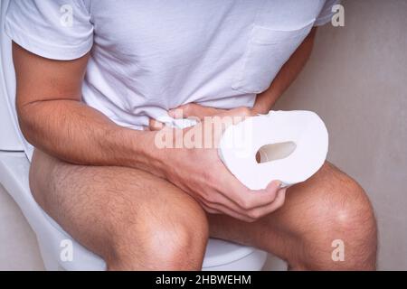 Man sitting on the toilet and suffering from stomach pain, constipation, diarrhoea or stomach cramps Stock Photo