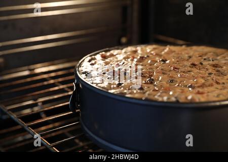 A close up large round traditional Christmas cake in the oven slowly baking or cooking. A variety of fruit visible on the still wet moist surface. Stock Photo