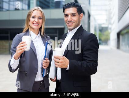 Businessman and his woman colleague in suit are standing with folder and coffee Stock Photo
