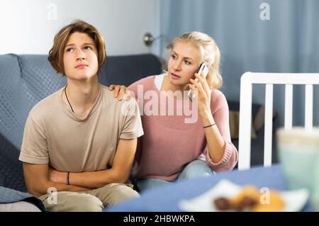 Woman sitting near her sad son and calling to doctor Stock Photo