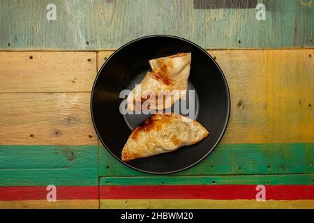 Top view image of Argentine chicken meat empanadas, one split in half to see the inner filling on a black plate Stock Photo