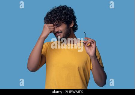 Tired curly-haired bearded guy suffering from eyestrain Stock Photo