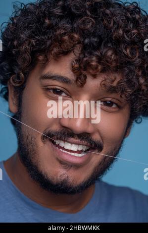 Pleased cute young man using dental floss Stock Photo