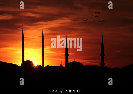 Sunset is down on minarets.Ramadan concept is with silhouette mosques on orange sky. Stock Photo
