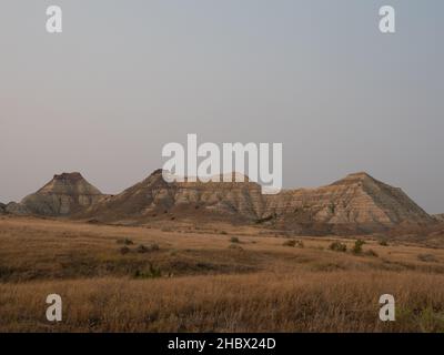 Striped barren hills of Terry Badlands, Montana, with field of dried grass and shrubs in foreground. Image photographed in golden hour. Stock Photo
