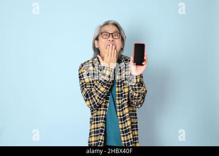 The senior Asian man with yellow plaid shirt standing on the blue background. Stock Photo