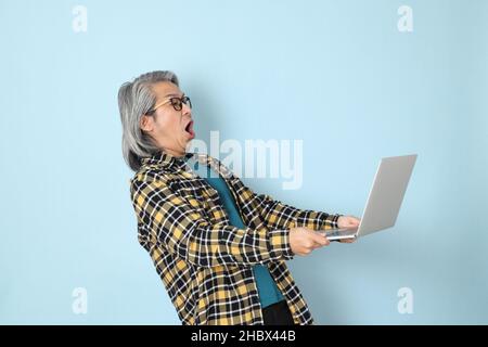 The senior Asian man with yellow plaid shirt standing on the blue background. Stock Photo