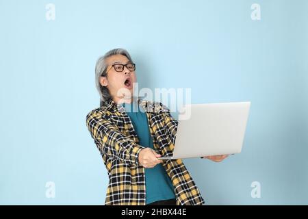The senior Asian man with yellow plaid shirt standing on the blue background. Stock Photo