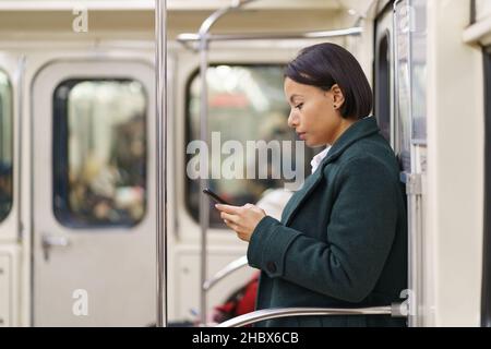 Sad afro american woman with smartphone in subway, tired female office worker using public transport Stock Photo