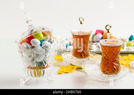 Colorful almond candies in the stylish,crystal candy bowl on the white table with Turkish Tea.The Sugar Feast end of Ramadan. Stock Photo