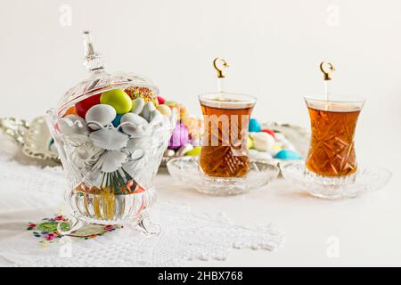 Colorful almond candies in the stylish,crystal candy bowl on the white table with Turkish Tea.The Sugar Feast end of Ramadan. Stock Photo