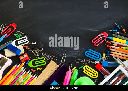 Colorful school supplies on the chalk dusty chalkboard with a large copy space.Education concept. Stock Photo