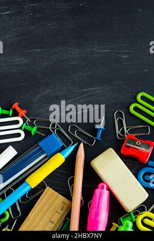 Colorful school supplies on the chalk dusty chalkboard with a large copy space.Education concept. Stock Photo