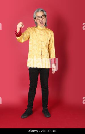 The senior Asian man wearing traditional gold chinese dresses standing on the red background. Stock Photo