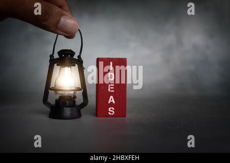 Looking for ideas concept. Hand holding vintage gas lamp and wooden tiles with text IDEAS Stock Photo