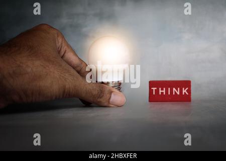 Creative thinking concept. Hand holding lightbulb and wooden cube with text THINK Stock Photo
