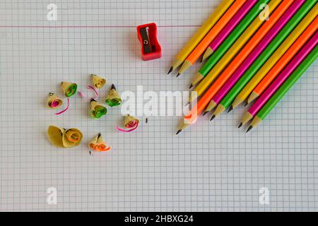 Fluorescent,neon color lead pencils on the checked paper background with waste and red sharpener. Stock Photo