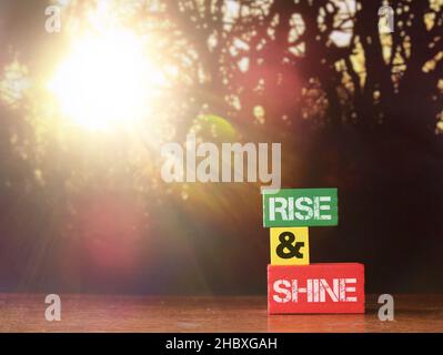 RISE AND SHINE written on wooden tiles with background of bokeh sunrise. Copy space for text Stock Photo
