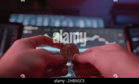Physical bitcoin shown in red light on stock chart monitor background Stock Photo